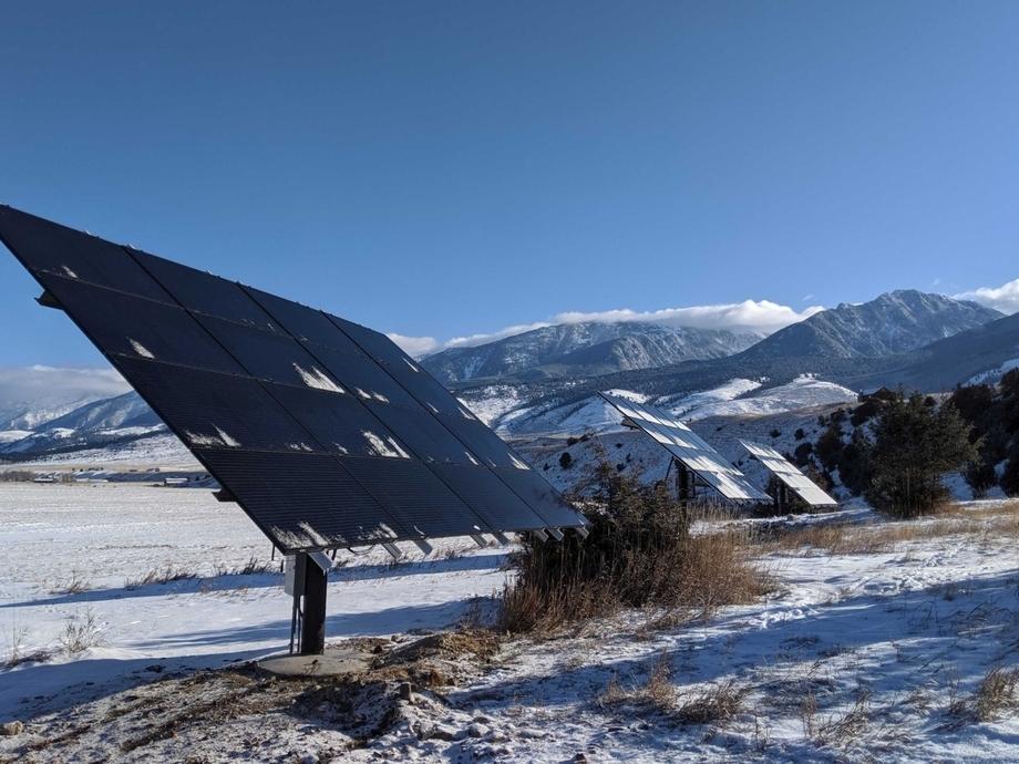 Residential ground mount solar array with snow on the ground and mountains behind.